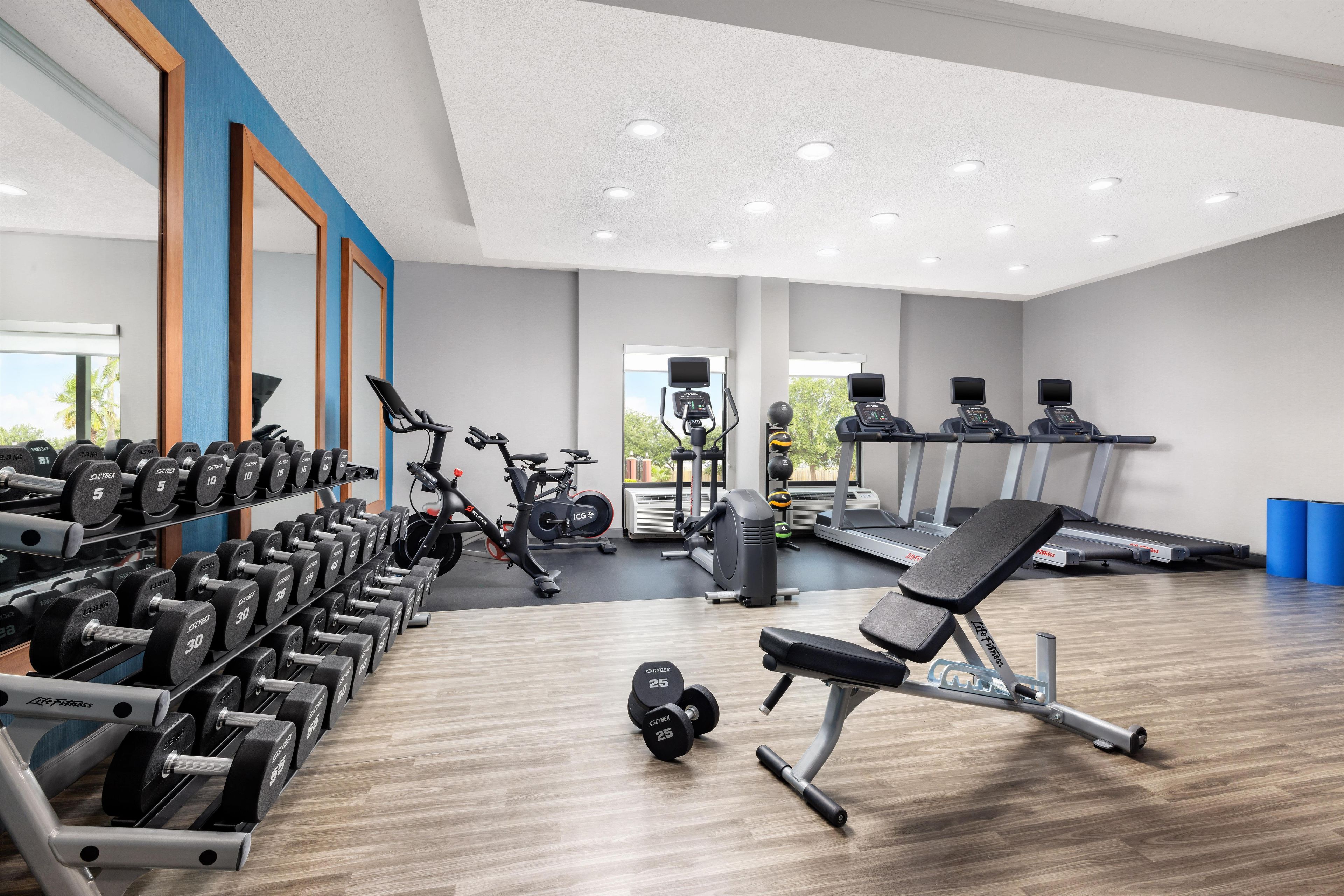 A gym with exercise equipment, mirrors, and a bench.