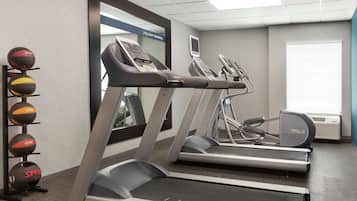 Een sportschool met loopbanden, een hometrainer en een aan de muur bevestigde televisie.