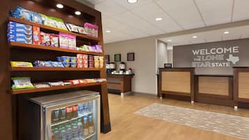A hotel lobby with a snack display, a refrigerator with beverages, and a welcome sign.