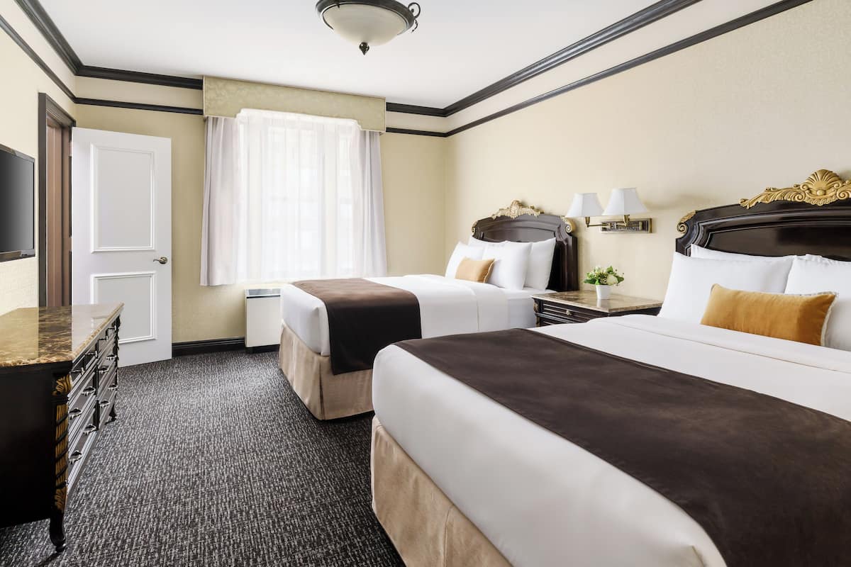 A hotel room with two beds, a desk, a television, and a window with curtains.