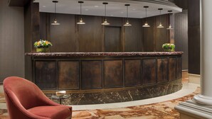 A reception area with a curved marble counter, a red upholstered chair, and a small table with a bowl.