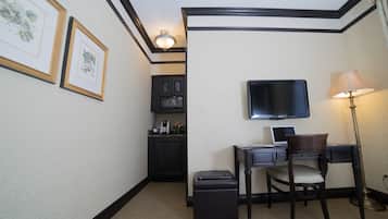 A hotel room with a desk, chair, television, lamp, and framed artwork on the wall.