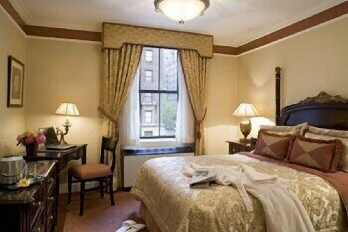 A hotel room with a bed, desk, chair, lamps, and a window with curtains.