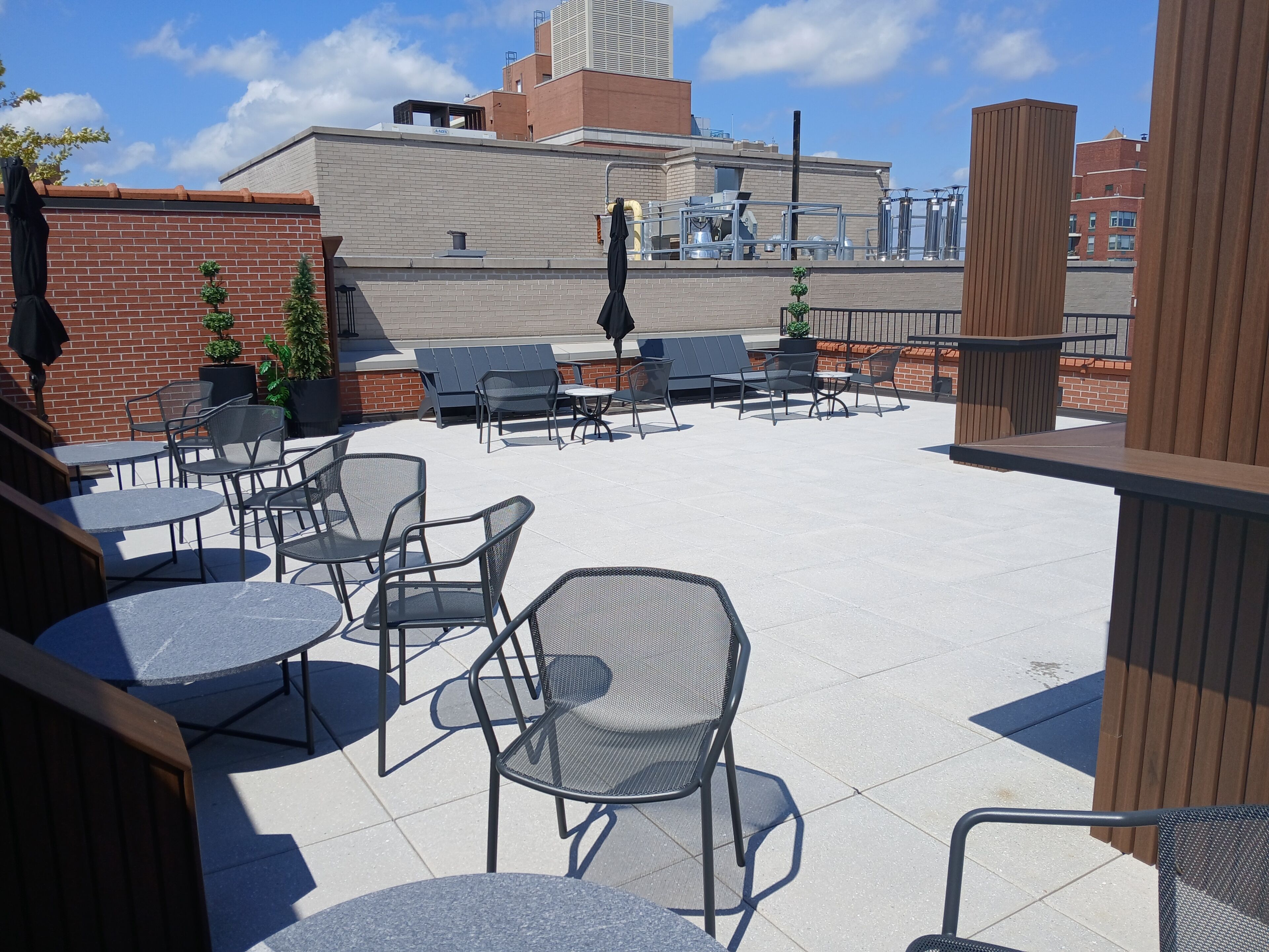 An outdoor patio with metal chairs and tables, brick walls, and a view of buildings in the background.