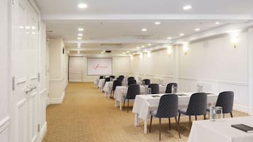 A conference room with rows of tables and chairs, a projector screen, and a carpeted floor.