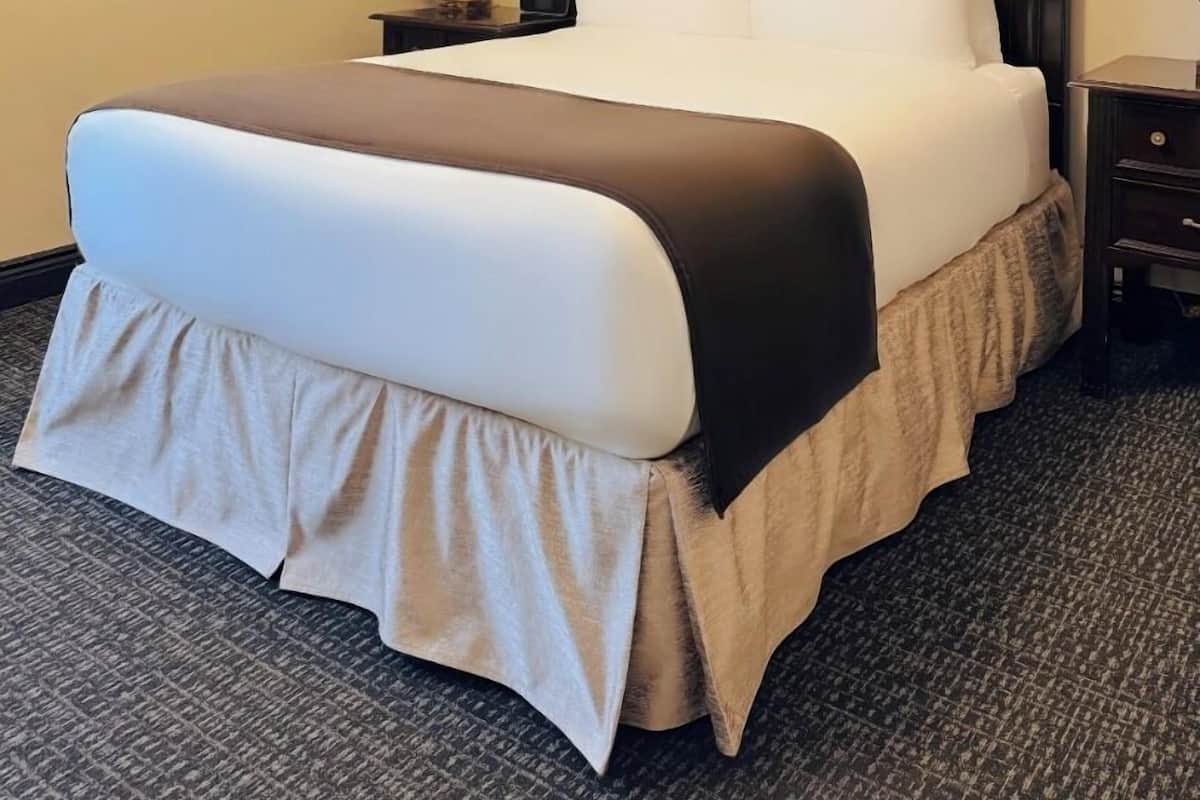 A neatly made bed with a dark headboard, a bedside table with a lamp, and a painting on the wall.