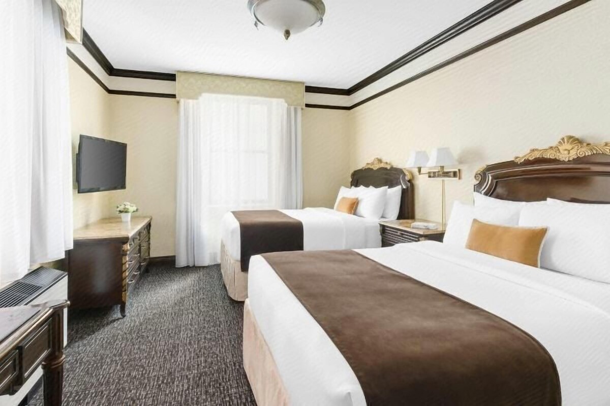 A hotel room with two beds, a desk, a television, and a window with curtains.
