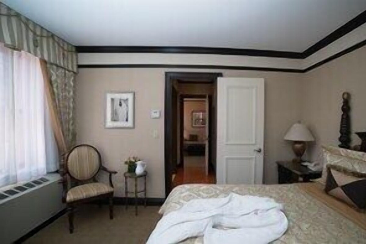 A hotel room with a bed, a chair, a lamp, and a door leading to another room.