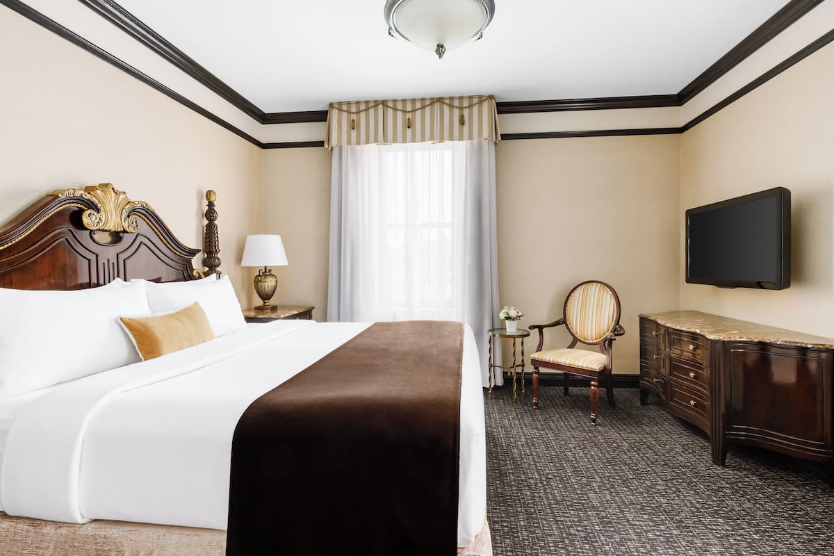 A hotel room with a large bed, a dresser, a television, and a chair.