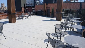 A rooftop patio with outdoor seating, a brick wall, and a view of the city skyline.