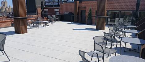 Un patio en la azotea con mobiliario exterior, un muro de ladrillo y vistas del horizonte de la ciudad.