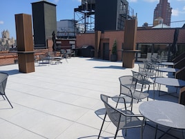 A rooftop patio with outdoor seating, a brick wall, and a view of the city skyline.