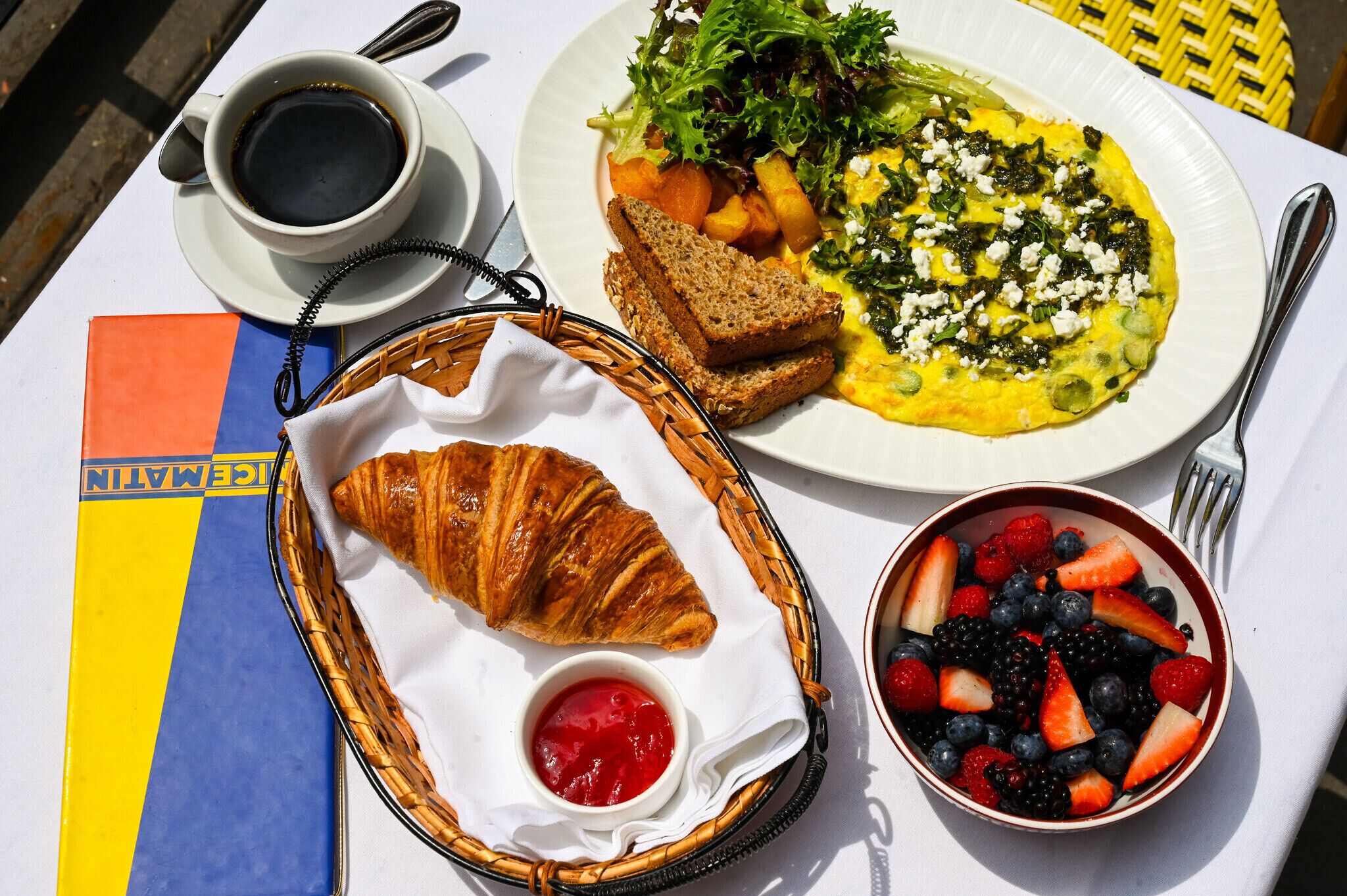 Desayuno con un croissant, un cuenco de bayas, un plato de huevos, tostadas y una taza de café.