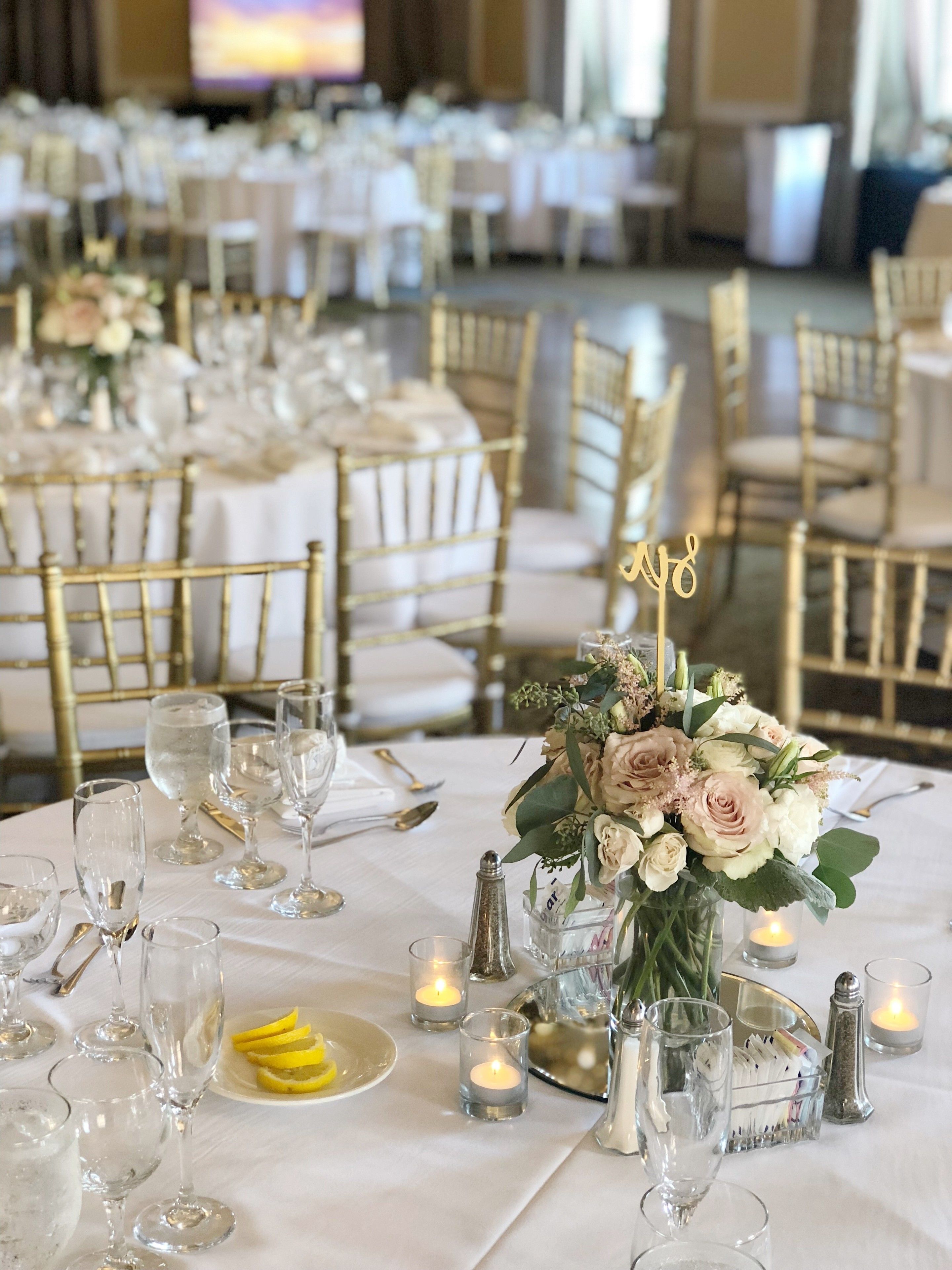 A banquet hall with round tables set for a formal event, featuring gold chairs, white tablecloths, and floral centerpieces.