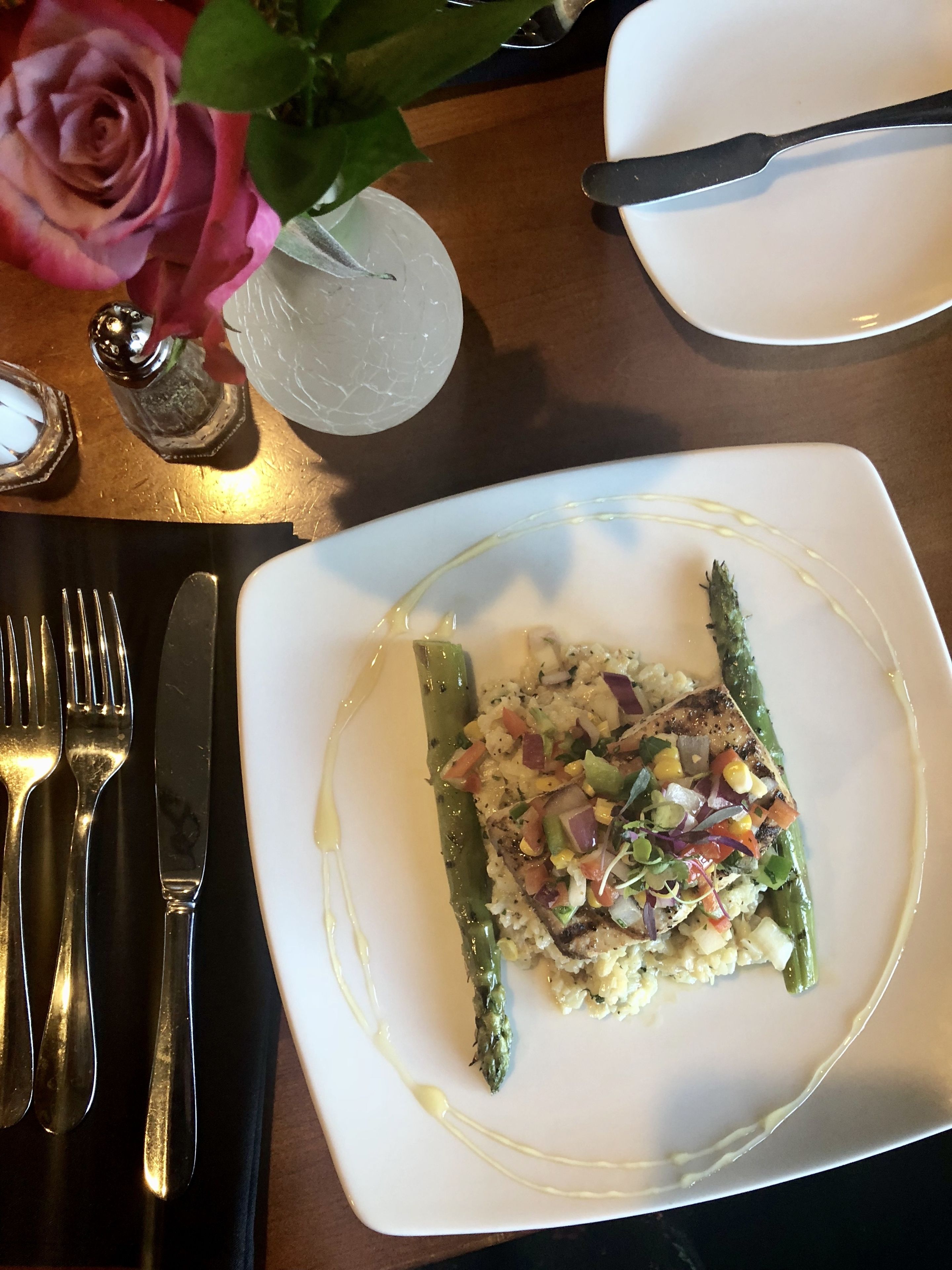 A white plate with a dish of asparagus and rice, accompanied by a fork and knife on a black napkin.