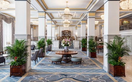 A grand lobby with a central round table, seating, and potted plants.