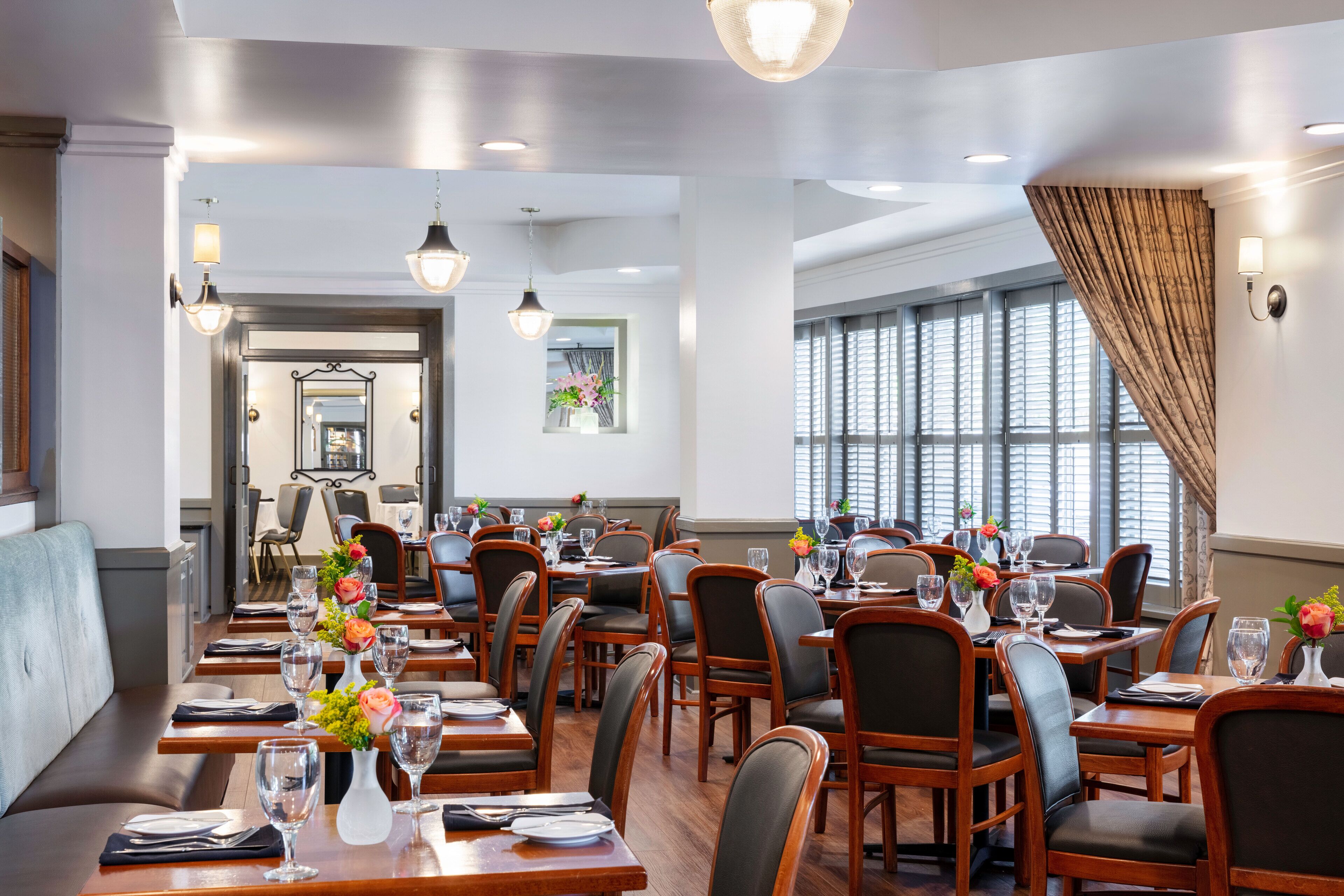 A restaurant with wooden tables and chairs, arranged in a spacious layout with large windows and a view of the outside.