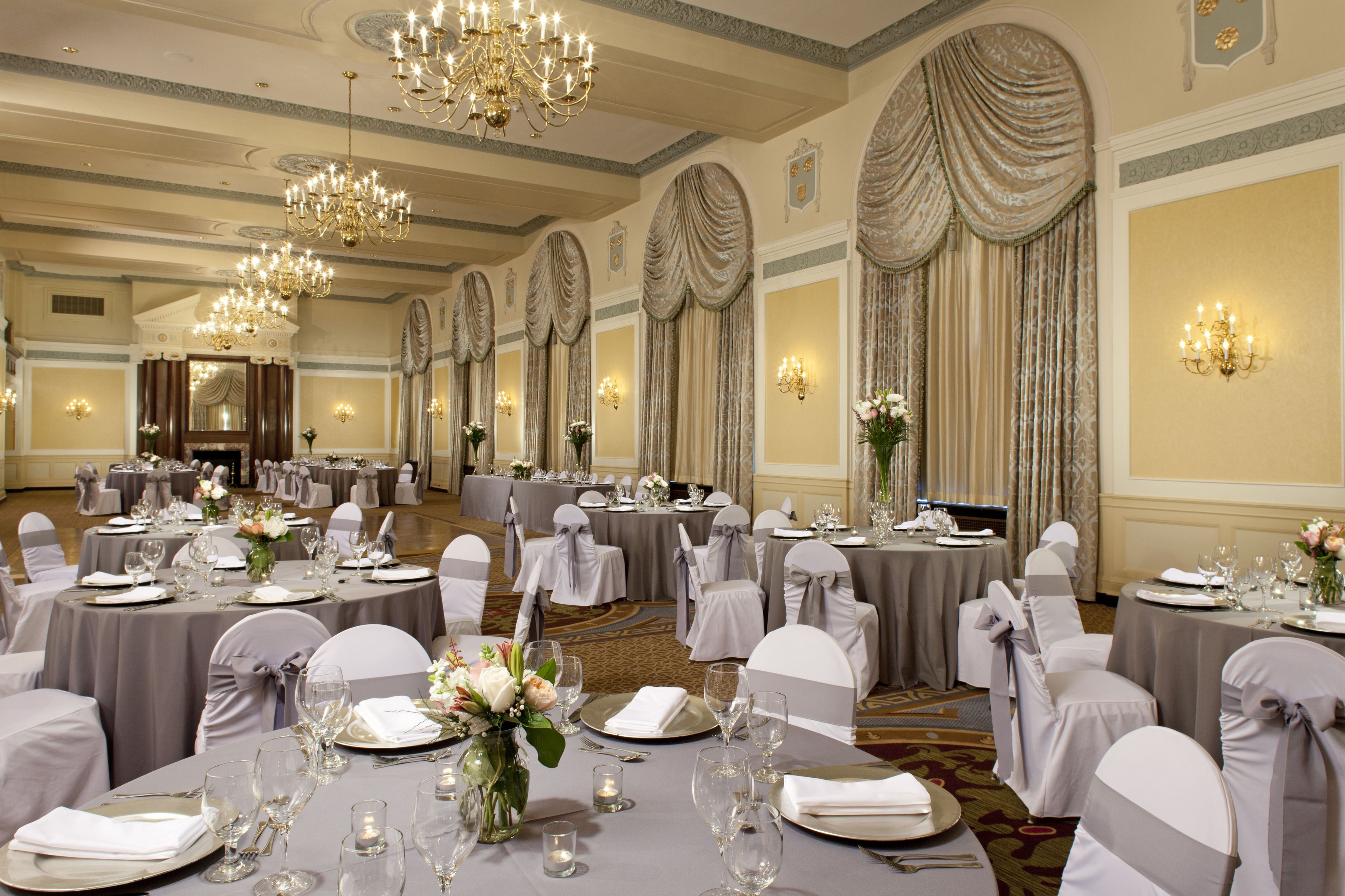 A banquet hall with round tables set for a formal event, featuring chandeliers and elegant drapery.
