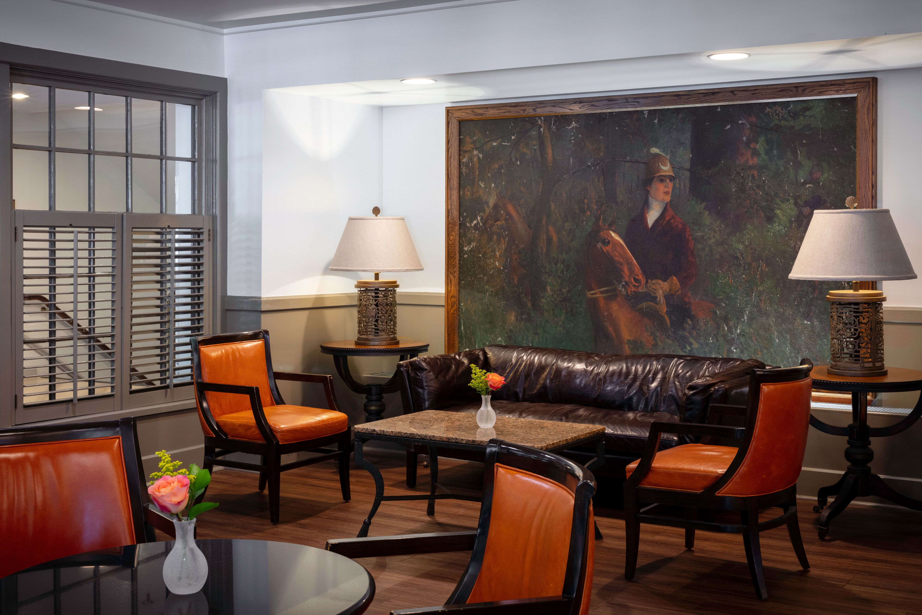 A room with a leather sofa, two chairs, a small table with a vase of flowers, and a painting on the wall.