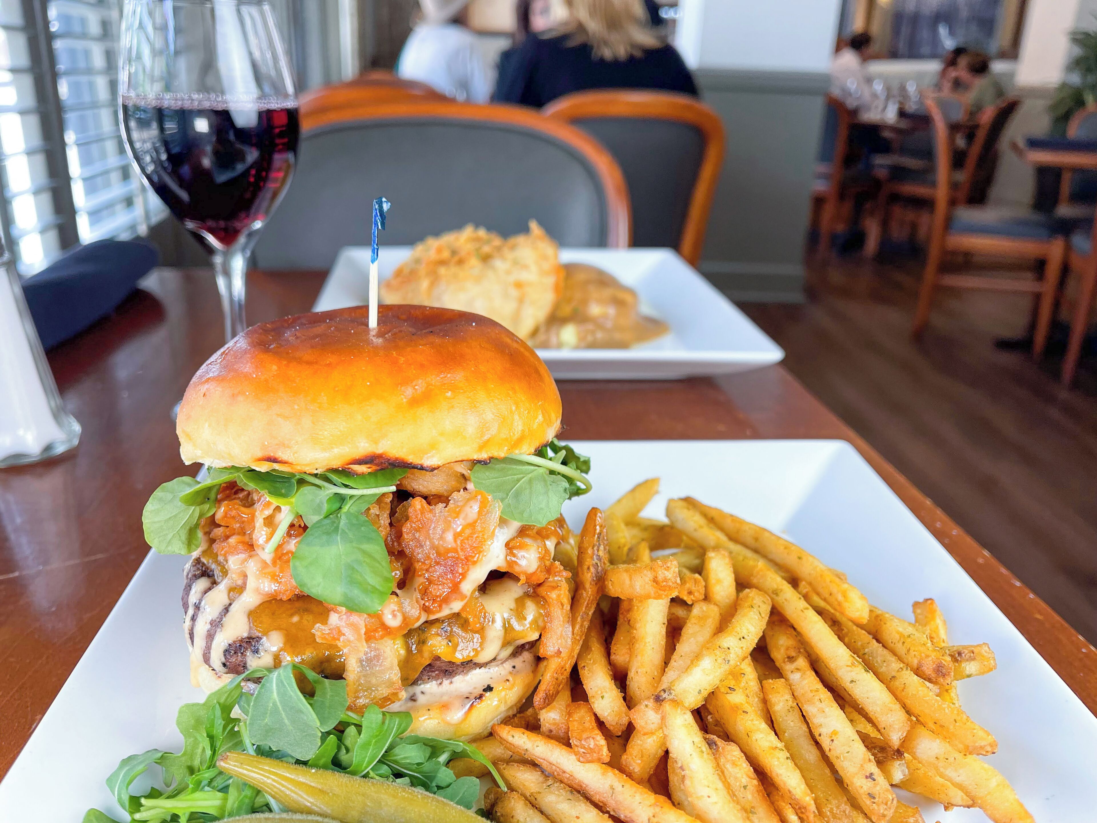 A plate with a burger and fries, a glass of red wine, and a seating area with tables and chairs.