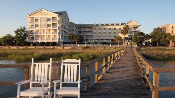 A wooden boardwalk leading to a hotel with multiple balconies and a view of the water.