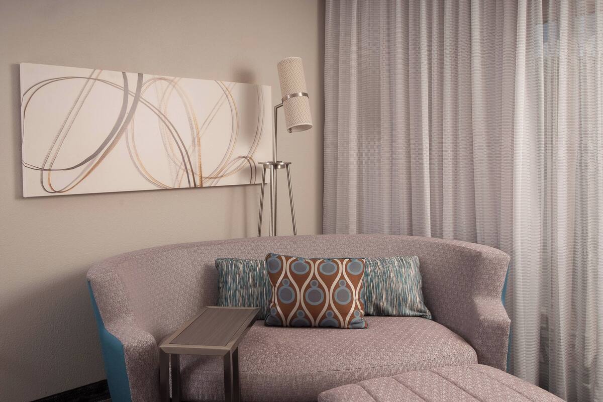 A modern living room with a sectional sofa, a small side table, a floor lamp, and a large abstract painting on the wall.