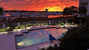 A swimming pool with lounge chairs and a view of a marina at sunset.