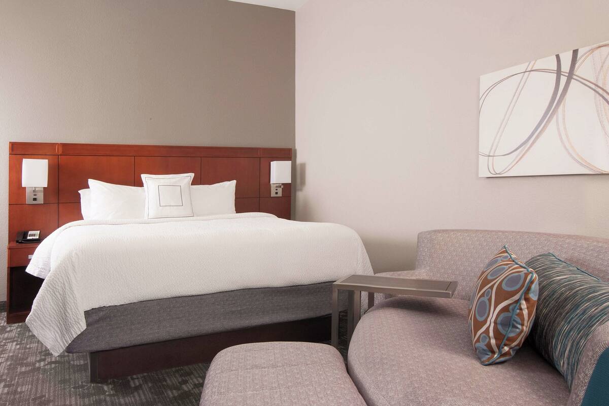 A hotel room with a bed, a sofa, a small table, and a wall-mounted artwork.