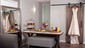 A dining area with a table set for a meal, a bench, a mirror, and a hanging wedding dress.