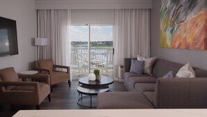 A modern living room with a sofa, armchairs, a small round table with decorative items, and a large window with a view of a marina.