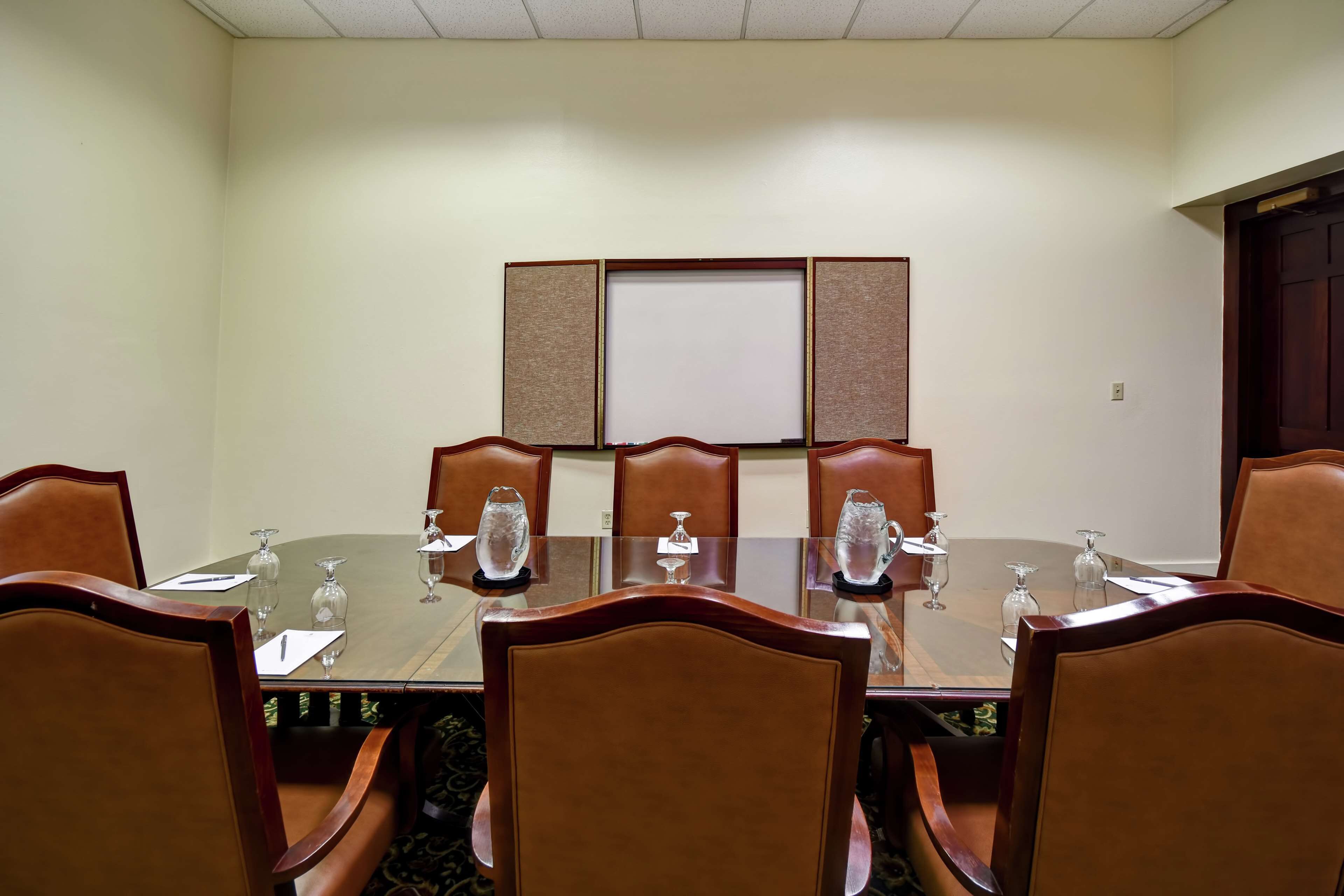 A conference room with a round table, six chairs, and a whiteboard on the wall.