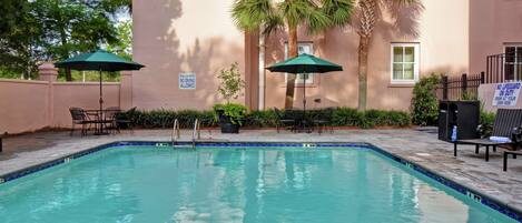 A swimming pool with two umbrellas, a lounge chair, and a sign indicating no lifeguard on duty.