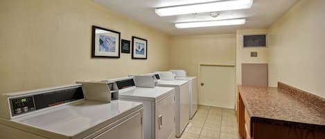 A laundry room with three stacked washers and dryers, a wooden counter, and a door leading to another room.