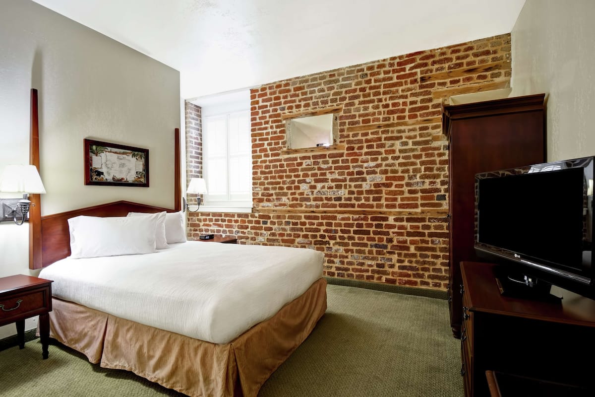 Camera d'albergo con parete in mattoni a contrasto, un letto grande, una televisione e una finestra con tende.