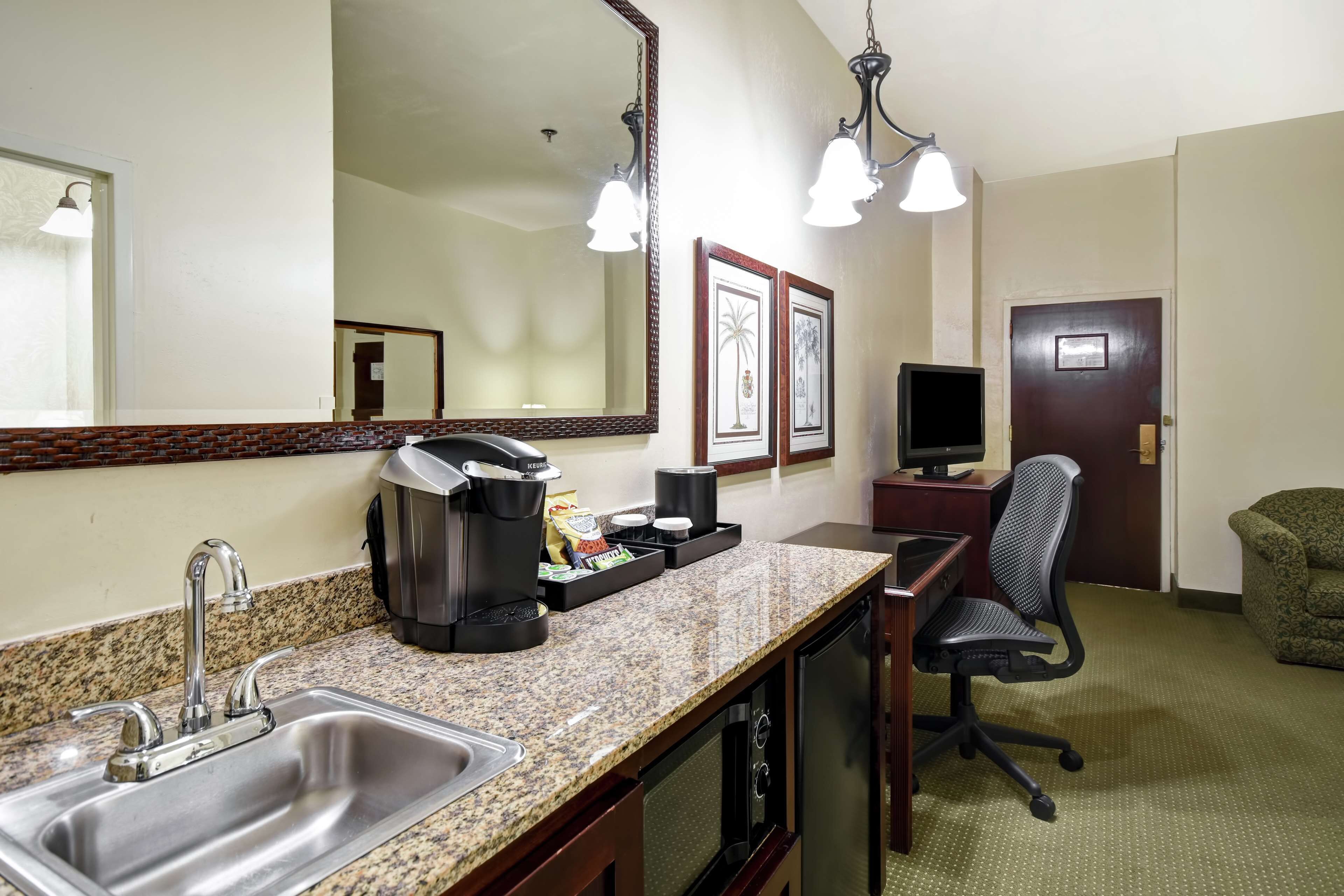 Habitación de hotel con encimera de granito, cafetera, televisor, una silla y una puerta.