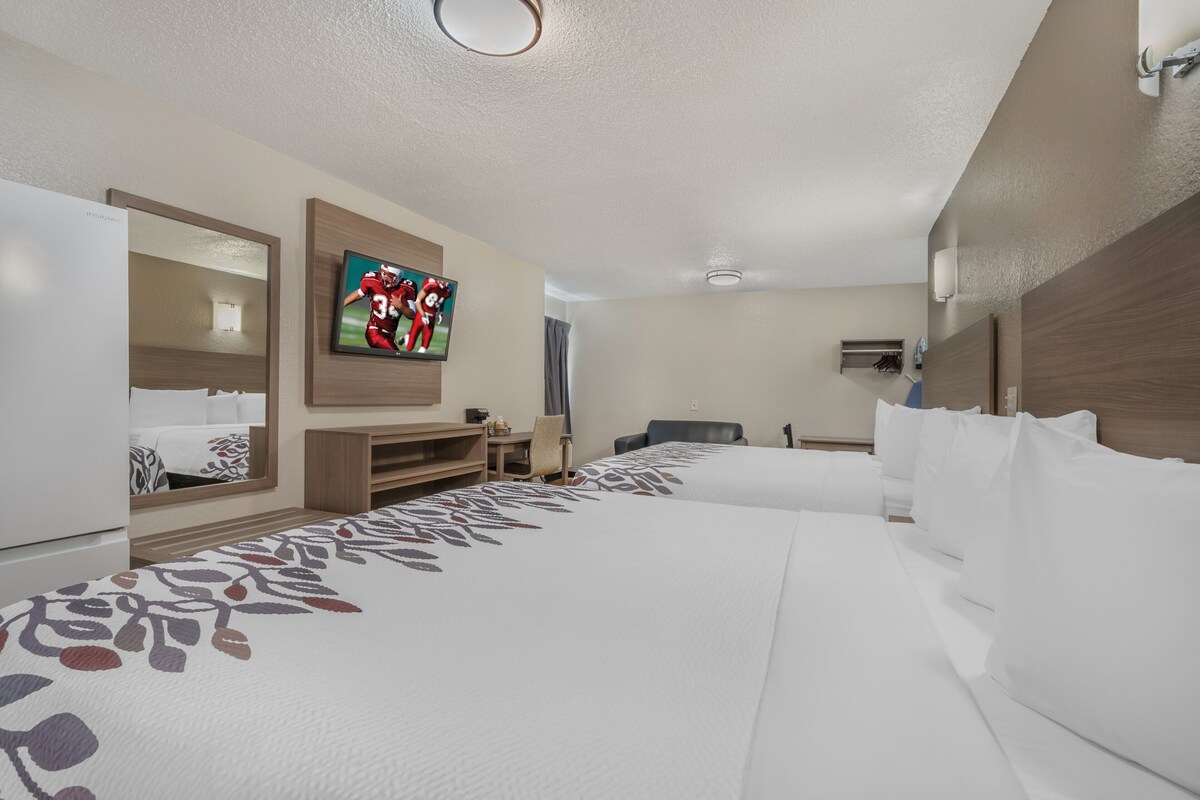A hotel room with a large bed, a TV mounted on the wall, a desk with a chair, and a mirror.