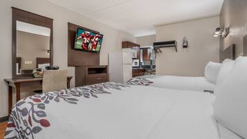 A hotel room with two beds, a TV, a desk, and a kitchenette.