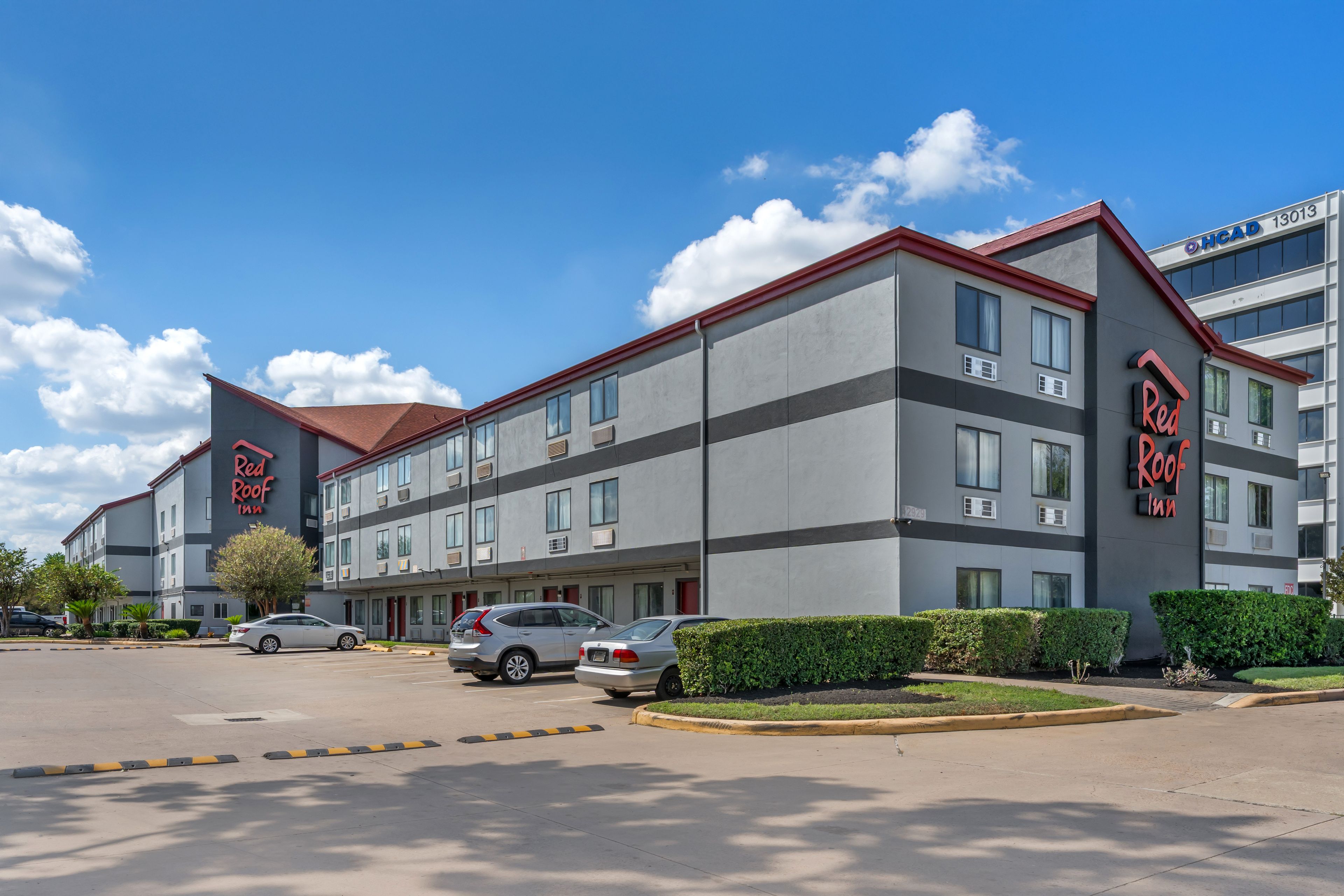 A Red Roof Inn hotel with a parking lot, multiple cars, and a clear blue sky.