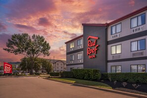 A Red Roof Inn hotel with a modern design, featuring multiple windows and a clear sky with clouds.