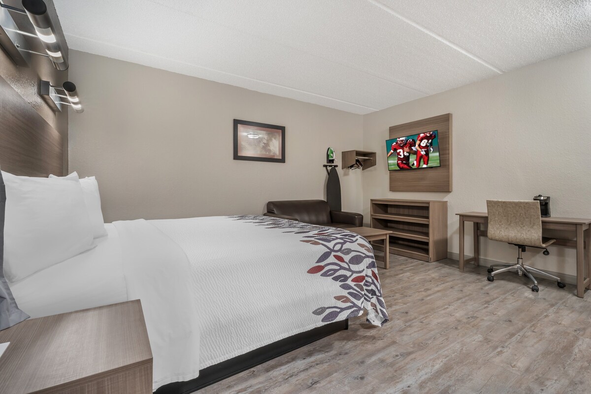 A hotel room with a bed, a desk, a chair, a TV, and a picture on the wall.