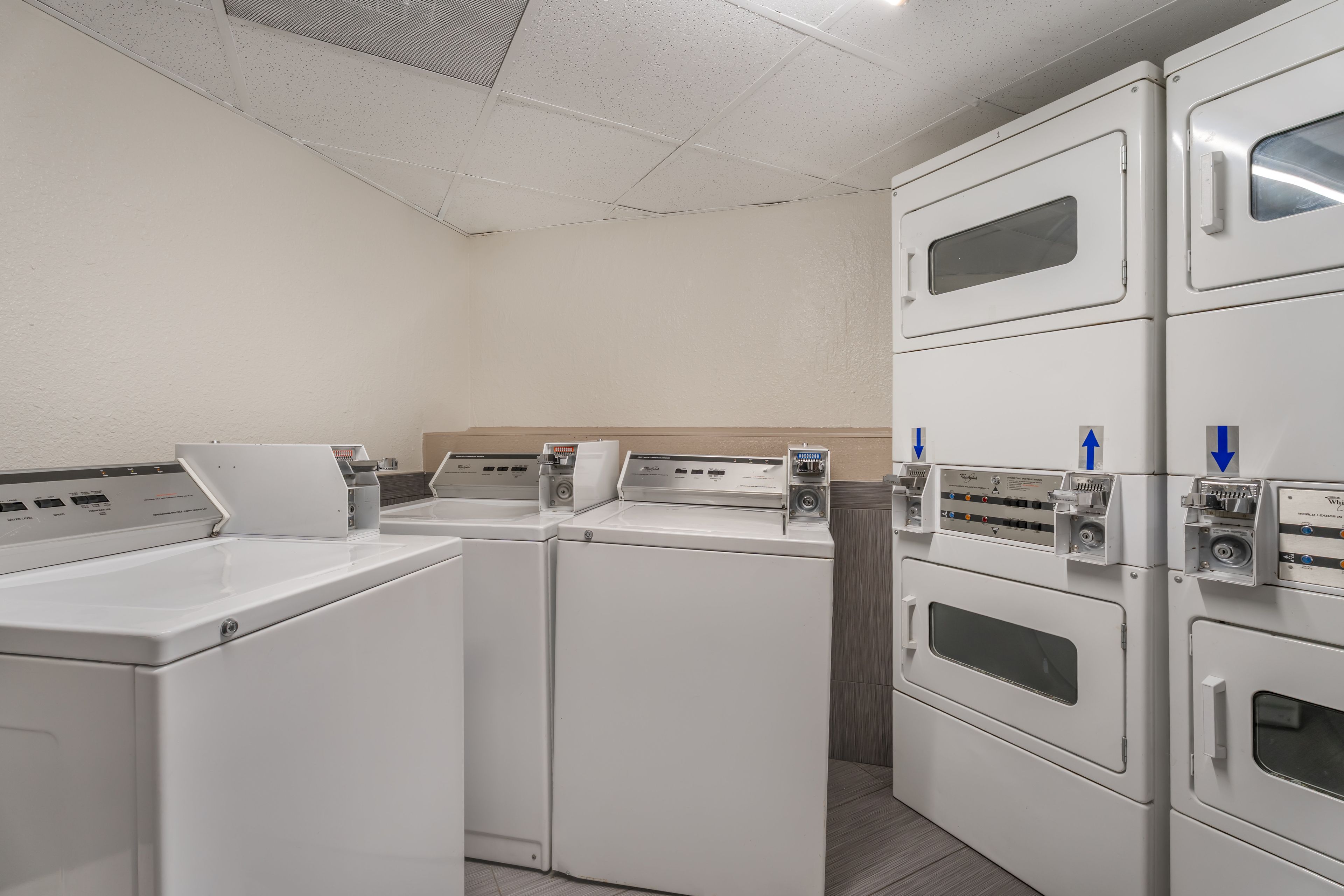A laundry area with stacked washers and dryers, control panels, and directional arrows on the machines.