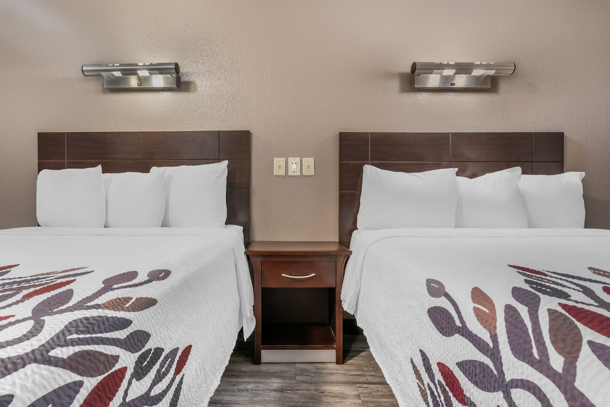 A hotel room with two beds, a nightstand, and wall-mounted lighting.