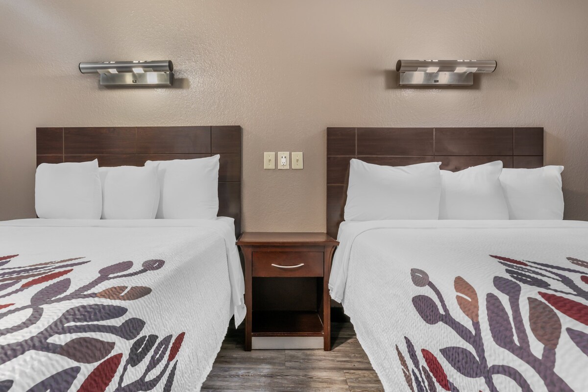 A hotel room with two beds, a wooden nightstand, and wall-mounted sconces.