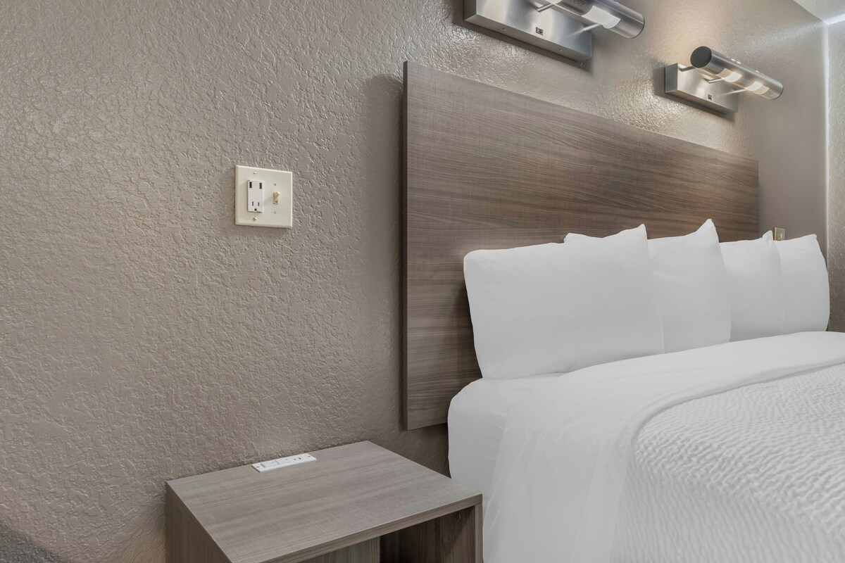 A hotel room with a textured wall, a wooden headboard, a bedside table, and a wall-mounted light fixture.