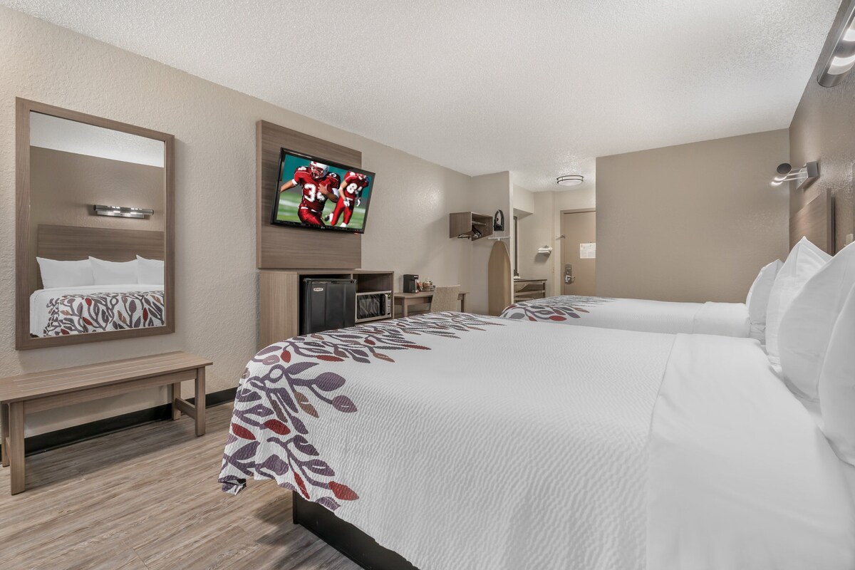 A hotel room with two beds, a TV, a desk, and a mirror.