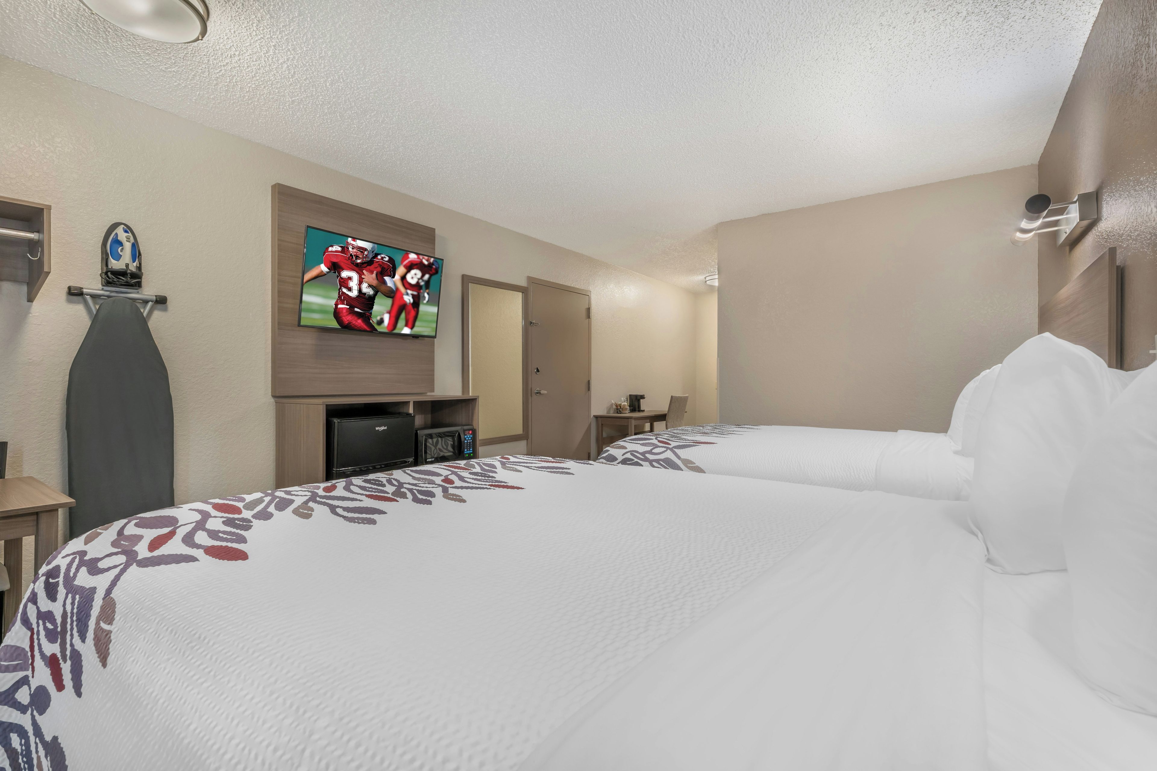 A hotel room with two beds, a flat-screen TV, a desk, and a door.