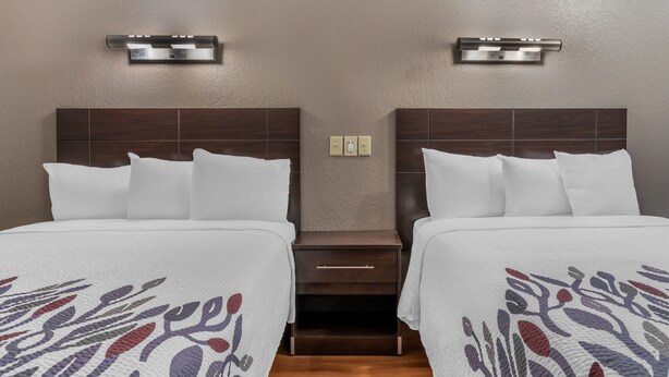 A hotel room with two beds, each with a headboard, a nightstand, and a wall-mounted light fixture.