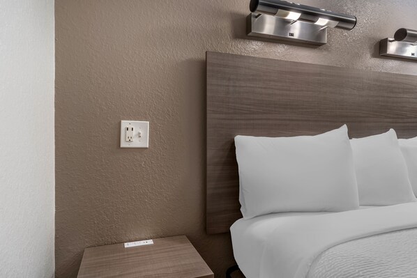 A hotel room with a bed, a nightstand, and a wall-mounted light fixture. - Red Roof Inn Houston - Brookhollow (Houston)