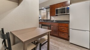 A compact kitchen with wooden cabinets, a stainless steel microwave, and a white refrigerator.