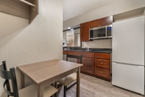 Cocina compacta con armarios de madera, un microondas de acero inoxidable y un refrigerador blanco.